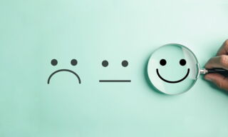 Drei Smiley-Gesichter vor leicht grünem Hintergrund - enttäuscht, mittel, zufrieden